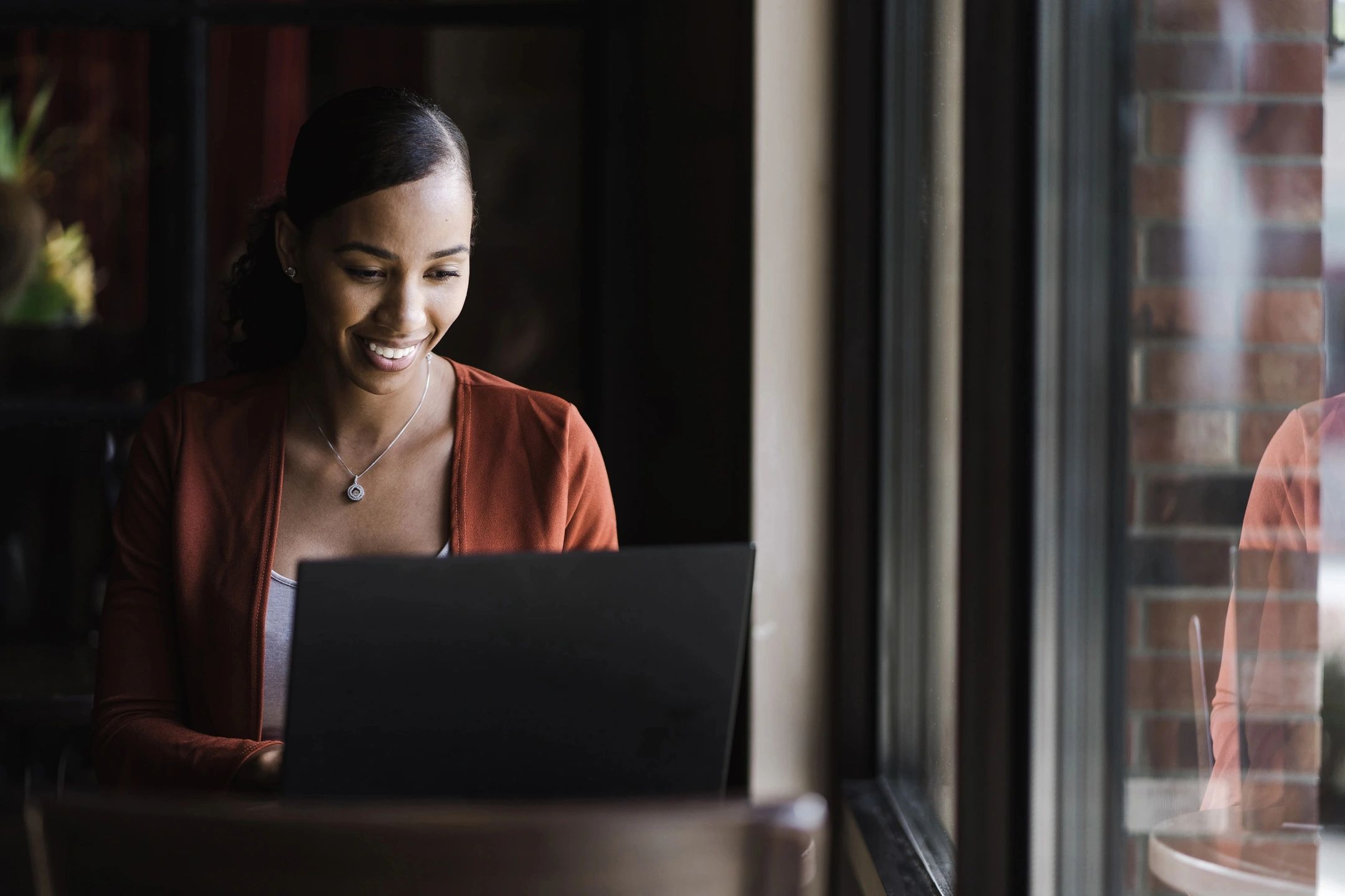 Woman sat next to window smiling at laptop