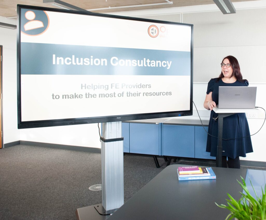 Helen Redmanan wearing a blue dress. She is in front of a display screen with reads'Inclusion Consultancy'.