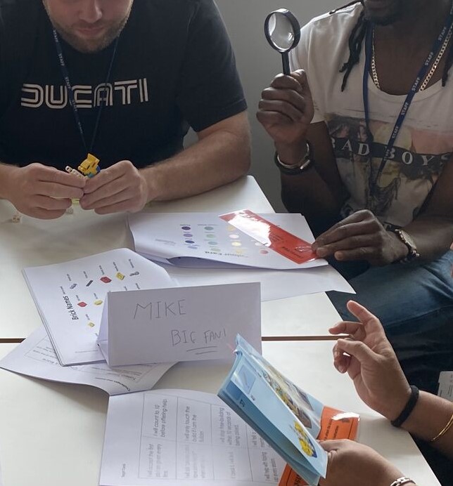 Group of adults with Lego resources. Sign reads 'Mike, big fan!'