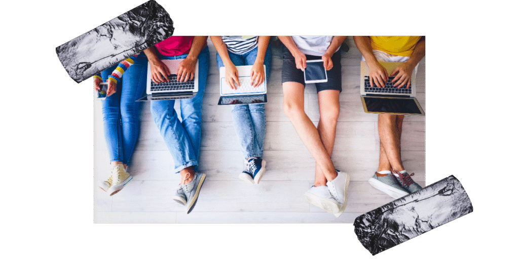 Image shows 5 pairs of young people's legs whilst they are sitting on the floor and leaning against a wall. each person has a laptop, phone or tablet.